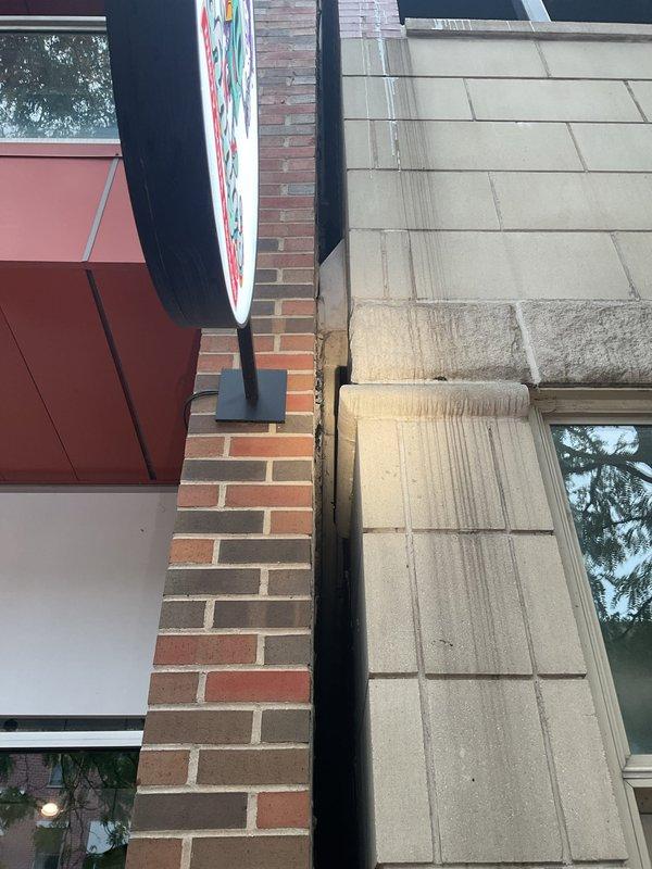 Performed a water leak locate to investigate reported moisture infiltrating the main entryway, suspected to originate from the unit porch drain. Visual inspection of the building exterior at the brick-to-limestone junction revealed significant water runoff staining and streaking below the projecting stone ledge, along with debris in the expansion joint, indicating exterior envelope water intrusion rather than a failure of the porch drain. Findings documented with photographs for repair planning and recommended sealing of the joint and ledge to prevent further water migration.