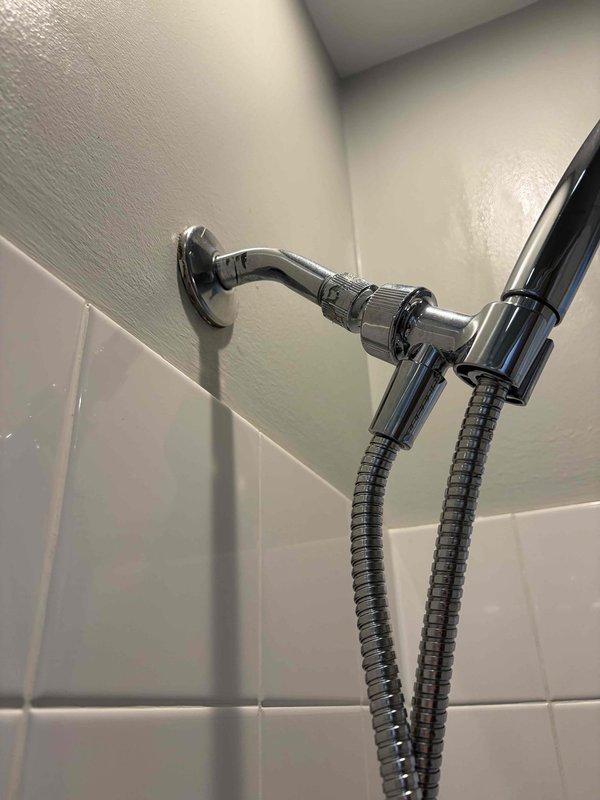 Responded to a reported slow drip at the bathtub and performed a leak locate. Inspected the shower arm, escutcheon, and handheld diverter mount and found no visible leaks or damage, then removed the tub overflow cover plate and found the linkage hardware and washers coated in deteriorated sealant and mineral buildup, indicating the overflow assembly as the probable leak source.
