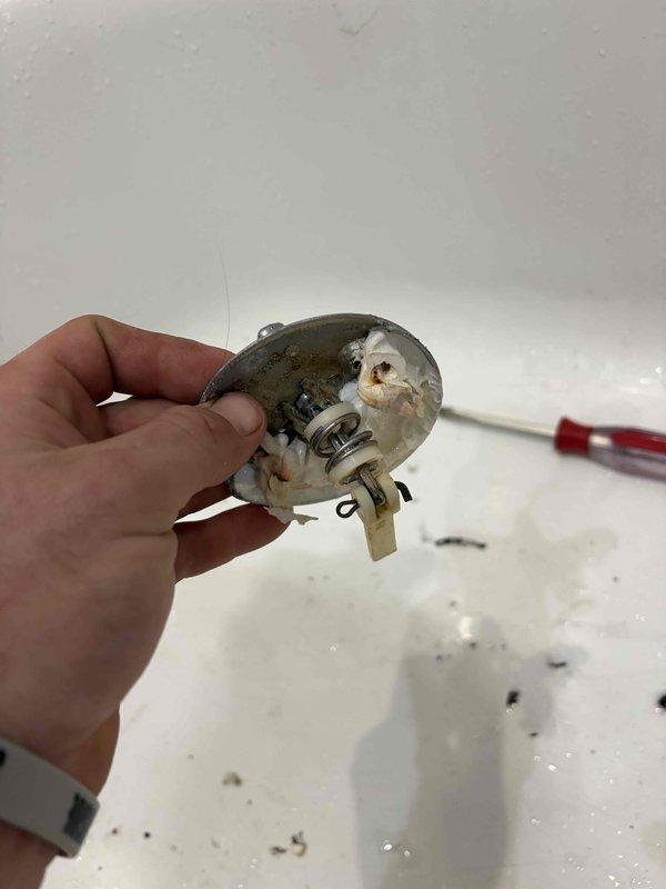 Responded to a reported slow drip at the bathtub and performed a leak locate. Inspected the shower arm, escutcheon, and handheld diverter mount and found no visible leaks or damage, then removed the tub overflow cover plate and found the linkage hardware and washers coated in deteriorated sealant and mineral buildup, indicating the overflow assembly as the probable leak source.