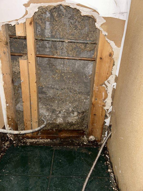 Inspected the dishwasher area for a reported leak and opened the adjacent wall cavity, exposing the copper supply lines and degraded insulation. Examined the sink base cabinet and drain assembly, finding long-term moisture damage with swollen, stained OSB flooring and water-streaked particleboard panels around the P-trap, tailpiece, and flexible supply line connections.