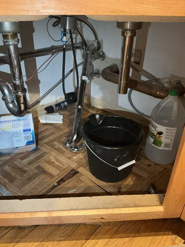 Inspected the under-sink drain assembly for a clogged fixture and found a cracked slip-joint lock nut on the tubular P-trap piping, along with moisture-related deterioration of the cabinet floor from the leaking connection. Removed the failed fitting for evaluation and staged the area for repair; the existing tubular drain piping requires full replacement, which is scheduled to be completed on a return visit.