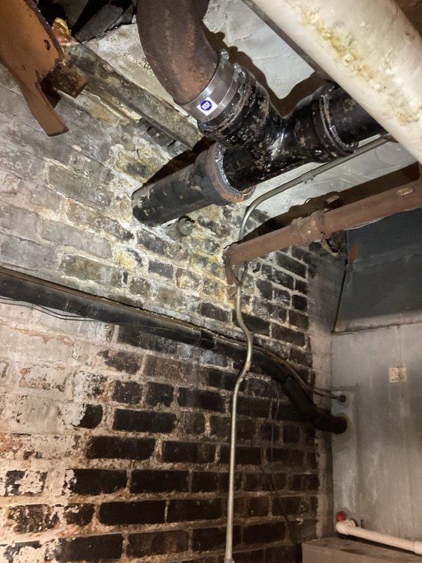 Responded to a warranty call regarding a suspected leak at a basement sanitary stack previously replaced. Inspected the cast-iron stack, clamp-style no-hub couplings, and adjacent drain piping, and documented existing conditions with photos, including heavy corrosion, staining, and soot on the surrounding piping and masonry, to support the warranty determination.