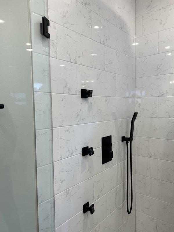 Inspected the master bathroom shower and kitchen faucet location to assess scope for three customer-supplied fixture installations: kitchen faucet replacement, a longer rain shower arm extension, and a handheld showerhead replacement requiring a new slide bar/pole mount. Documented the existing ceiling-mounted matte black rainfall head, wall-mounted handheld bracket, and thermostatic valve configuration on tiled walls, noting all fixtures and surrounding tile are in good condition with no visible damage, and prepared estimates for the work.