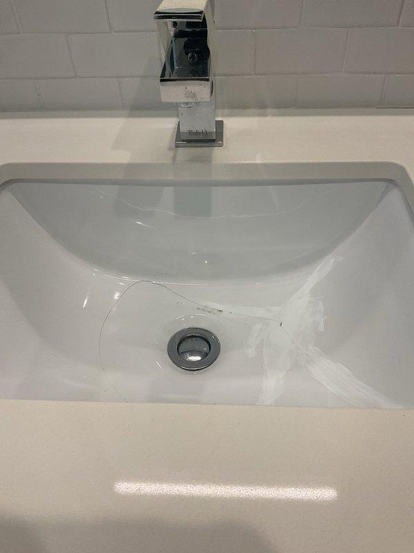 Inspected the cracked porcelain undermount bathroom sink basin and applied repair compound to the crack near the drain to seal the damage, with the chrome faucet and pop-up drain assembly left in place. Also patched the mortar around the exterior hose spigot penetration, restoring a sealed, weather-resistant joint at the brick wall.