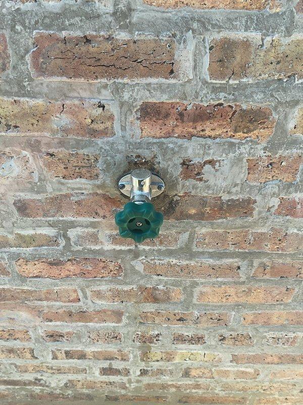Responded to a continuously dripping exterior hose bib and inspected the wall-mounted spigot, mounting flange, and surrounding masonry, where a damp area was observed on the concrete beneath the hose connection. Corrected the leak at the spigot, resecured the flange to the brick wall, and sealed the surrounding mortar joint to prevent moisture intrusion. Verified the fixture operates properly with no remaining drips or leaks.