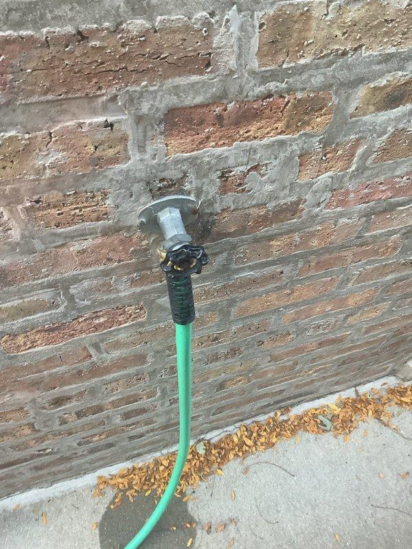 Responded to a continuously dripping exterior hose bib and inspected the wall-mounted spigot, mounting flange, and surrounding masonry, where a damp area was observed on the concrete beneath the hose connection. Corrected the leak at the spigot, resecured the flange to the brick wall, and sealed the surrounding mortar joint to prevent moisture intrusion. Verified the fixture operates properly with no remaining drips or leaks.