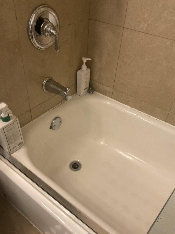 Cleared a clogged bathtub drain caused by organic debris, which had been aggravated by a prior attempt to treat it with chemical drain cleaner. Removed the obstruction and flushed the drain line, then confirmed the tub now drains freely, with the standing water draining through the chrome drain without backup. Inspected the surrounding fixtures and overflow plate and left the area clean.