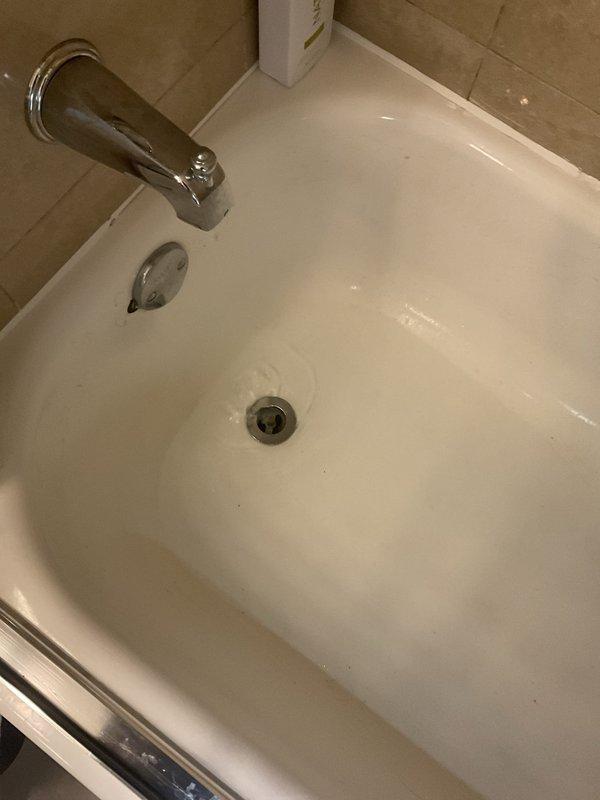 Cleared a clogged bathtub drain caused by organic debris, which had been aggravated by a prior attempt to treat it with chemical drain cleaner. Removed the obstruction and flushed the drain line, then confirmed the tub now drains freely, with the standing water draining through the chrome drain without backup. Inspected the surrounding fixtures and overflow plate and left the area clean.