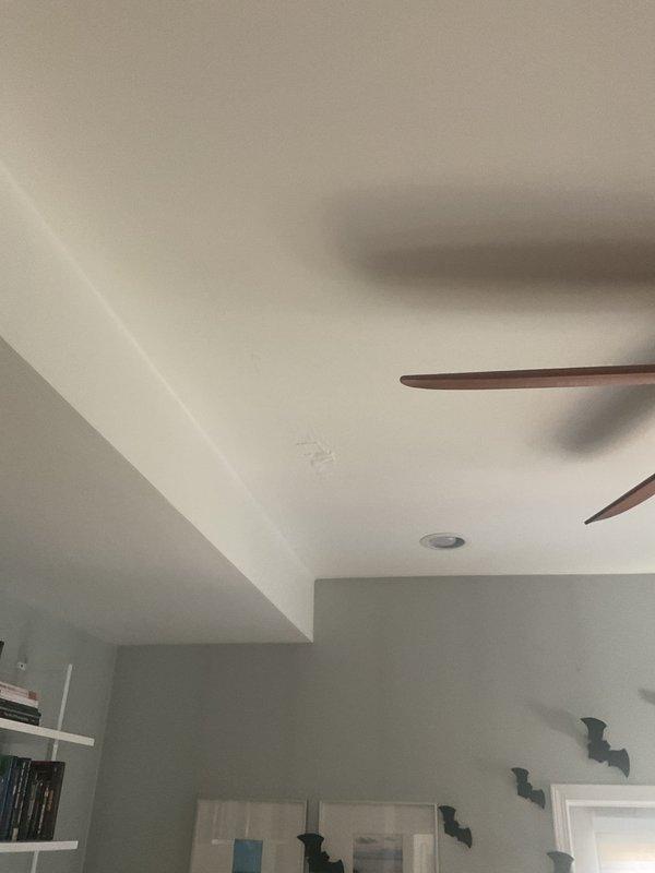 Performed a water leak locate investigation in response to reported moisture behind the bathroom wall, visually inspecting the tub surround, fixtures, and adjacent wall and floor areas. Documented evidence of moisture intrusion, including paint seam cracking at the wall-to-tub transition, staining on the floor tile near the tub and toilet, and ceiling discoloration in the adjacent room below, indicating a probable active leak in the tub-area supply or drain lines.