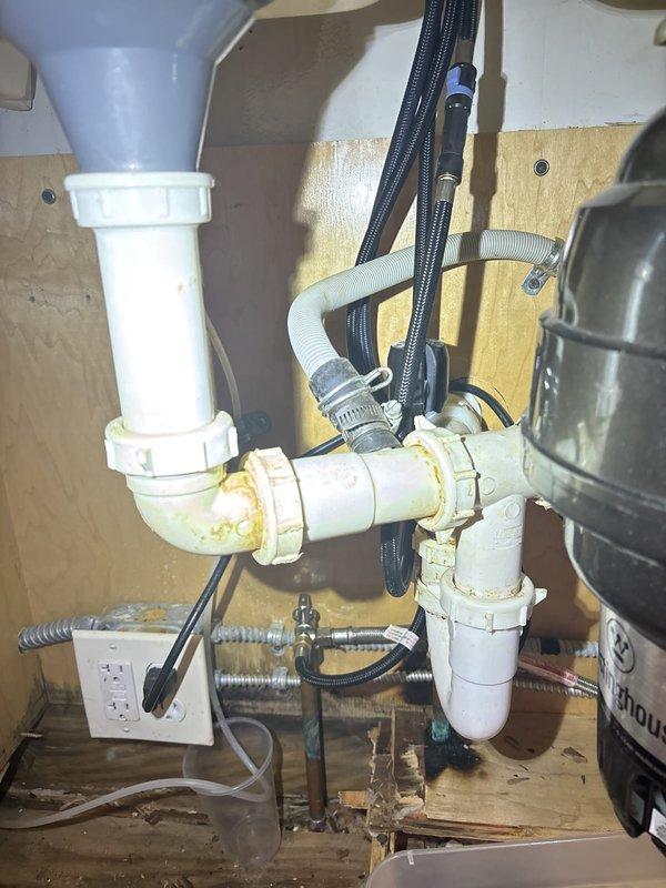 Inspected the under-sink drain assembly and garbage disposal and located the source of the leak at the slip-nut connections and elbow joint, where staining indicated prior seepage. Repaired the leaking drain connections to restore a watertight seal at the disposal discharge and P-trap, then tested under flow to verify no further leaks. Rotted cabinet flooring from long-term moisture exposure was noted, and the shower fixtures were checked and found intact with no visible damage.