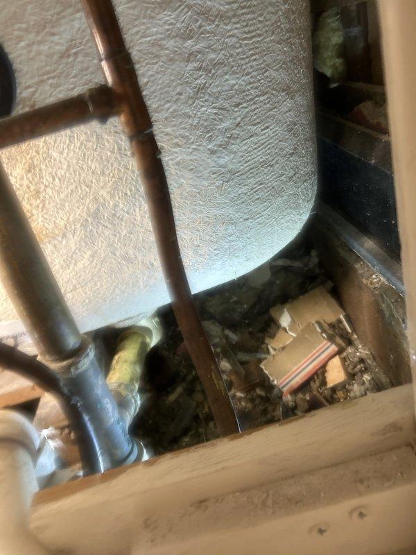 Performed a water leak locate investigation in response to dripping at the bathtub faucet and tub base, with water migrating down to the kitchen ceiling below. Inspected the affected ceiling area, documenting a water-stained ceiling tile section along the crown molding, and examined the adjacent mechanical space near the water heater, noting accumulated debris and exposed copper supply piping and fittings. Documented findings with photographs to support repair recommendations.