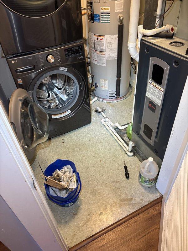 Responded to a laundry room floor drain backup with sewage overflow and inspected the drain line serving the floor drain. Exposed the floor drain connection, removing the corroded drain flange and broken concrete surround to access the PVC drain piping and metallic coupling, which contained heavy tar-like sludge buildup. Cleared the obstruction and cleaned out the debris, leaving the PVC assembly and fittings open for repair of the damaged drain connection.