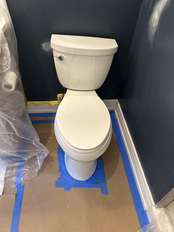 Inspected the loose toilet and accessed the tank interior to evaluate the internal components and mounting hardware. Retightened the fixture to secure it to the floor flange, and the bathroom was protected with floor covering and plastic sheeting throughout the work.