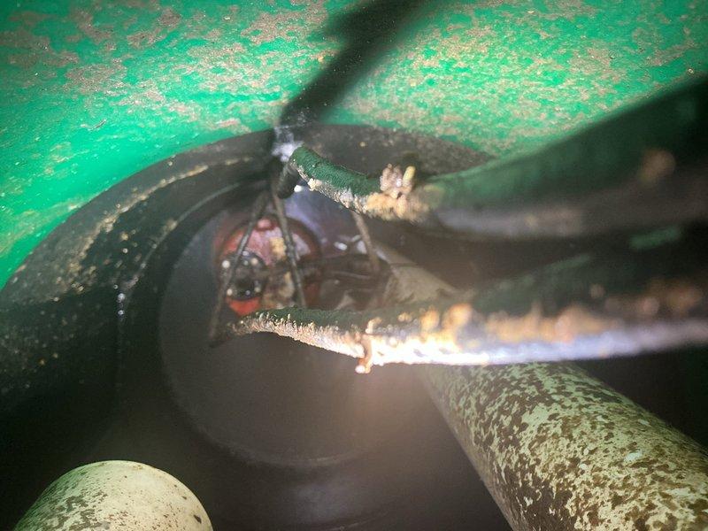 Inspected the ejector pit and adjacent drain connections to identify the source of recurring drain fly activity. Observed heavy corrosion and mineral buildup on the pit's internal components and discharge piping, along with debris and gaps at the floor penetration around the PVC drain and fittings, which provide breeding conditions for drain flies. Evaluated the pit and surrounding drain lines and documented findings with photos, with recommendations to clean and sanitize the pit, service the corroded components, and seal the penetration to prevent recurrence.