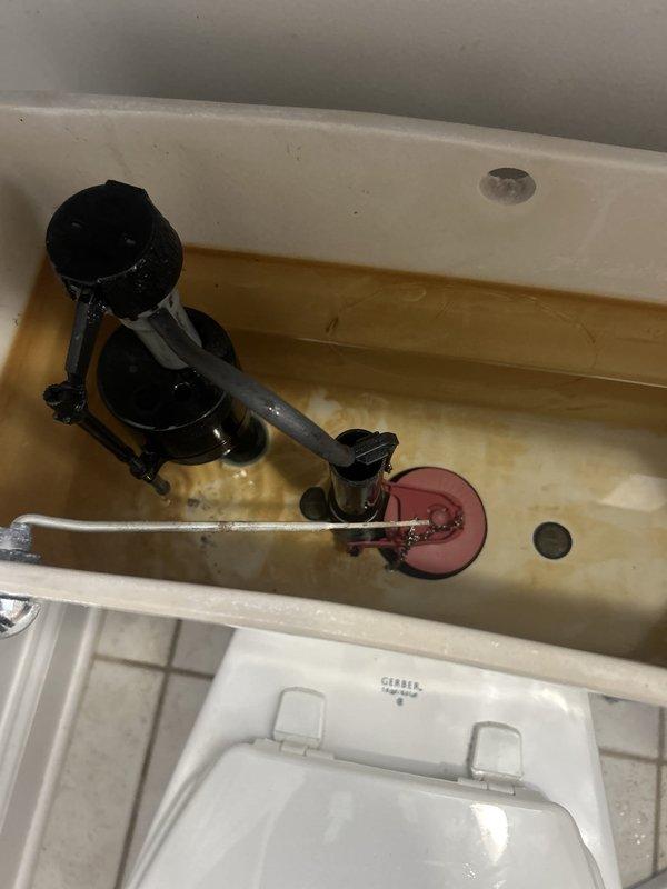 Replaced the fill valve and flapper in a standard gravity-fed toilet using materials stocked on the service vehicle. The tank interior showed heavy mineral and rust staining, and the old components were removed and the new fill valve and flapper installed. Water level was adjusted, and the flush cycle and refill were tested to confirm proper operation with no running water or leaks.