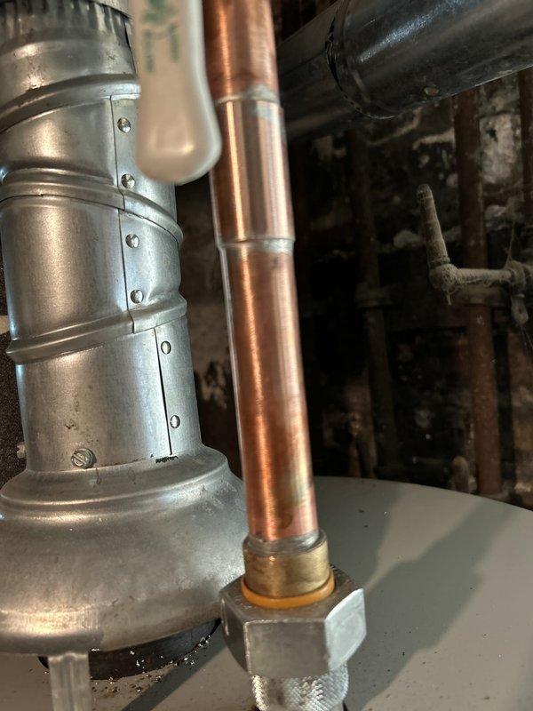 Responded to a reported leak at a union connection from a recent repipe and inspected the copper supply piping at the water heater. Found heavy corrosion and mineral buildup at the brass fitting and nipple on the cold water inlet, with rust staining on the tank top and dampness near the flue collar. Isolated the water supply and addressed the leaking connection to restore a watertight seal.