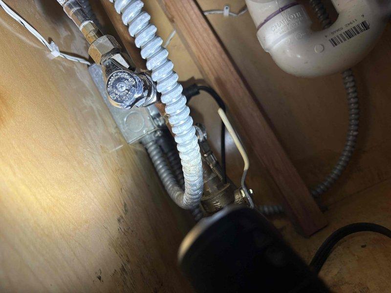Inspected the kitchen sink faucet and under-sink cabinet for the reported leak, checking the pull-down faucet hose and spray head, the chrome angle-stop valve, the flexible supply line connections, and the PVC P-trap drain assembly. No active leaks, corrosion, or component damage were observed at the supply or drain connections, and the area was left clean and functional.