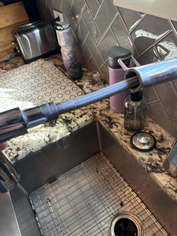 Inspected the kitchen sink faucet and under-sink cabinet for the reported leak, checking the pull-down faucet hose and spray head, the chrome angle-stop valve, the flexible supply line connections, and the PVC P-trap drain assembly. No active leaks, corrosion, or component damage were observed at the supply or drain connections, and the area was left clean and functional.