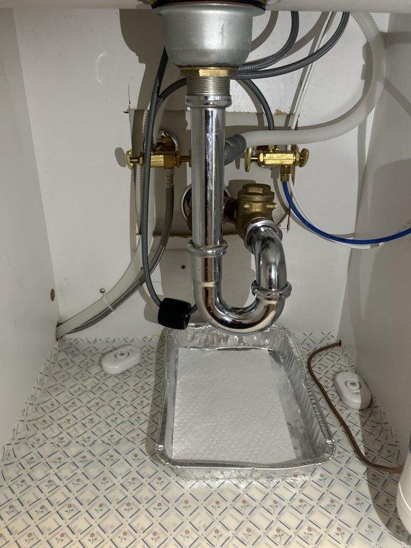 Inspected the under-sink drain assembly and supply connections following a reported leak after a kitchen remodel. Examined the chrome P-trap, sink strainer connection, brass shutoff valves, braided supply lines, and filter plumbing, and found no active leaks, corrosion, or water damage; leak sensors and a drip tray were in place. Documented the condition of the installation with photos and provided an assessment of the drain configuration.