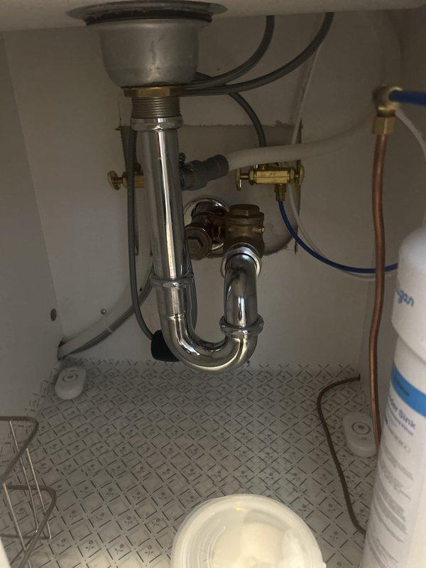 Inspected the under-sink drain assembly and supply connections following a reported leak after a kitchen remodel. Examined the chrome P-trap, sink strainer connection, brass shutoff valves, braided supply lines, and filter plumbing, and found no active leaks, corrosion, or water damage; leak sensors and a drip tray were in place. Documented the condition of the installation with photos and provided an assessment of the drain configuration.