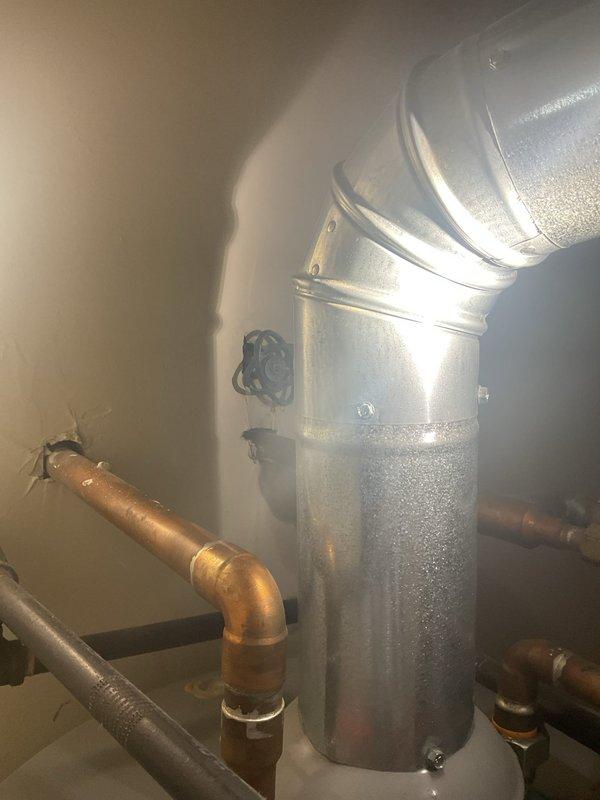 Inspected the reported shower leak and found water dripping from the chrome shower head at the arm connection, where an inline filter/adapter is installed between the shower arm and spray face. Evaluated the surrounding wall-mounted tile and the adjacent water heater closet, noting aging copper supply piping and flue components as part of the system assessment.