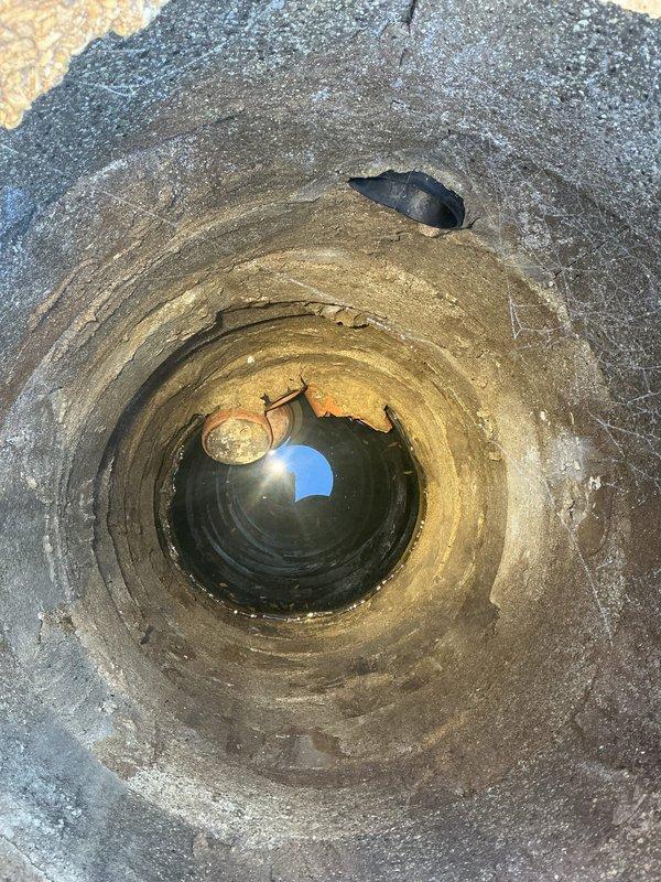 Performed a camera inspection of the drain system, accessing the line through a cut-in access opening in the wall to expose a heavily corroded cast-iron fitting with a hex-head cleanout plug showing significant rust scaling and mineral buildup. Also inspected a deep vertical shaft with layered masonry walls, observing standing water at the base with debris and an object partially visible near the bottom. Findings were documented with photos for further evaluation and recommendations.