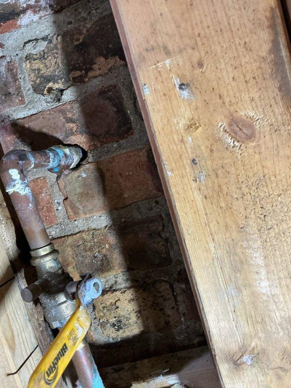 Assessed the kitchen supply piping to quote installation of a dedicated dishwasher shut-off valve. Inspected the existing copper supply line and in-line brass ball valve at the masonry wall penetration, noting corrosion, mineral buildup, and verdigris staining at the elbow and joints, along with a capped copper stub. Evaluated the cramped, cluttered work area and prepared the estimate for the independent isolation valve.