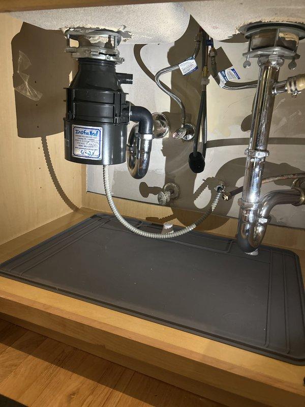 Removed the jammed garbage disposal and installed a new unit, connecting it to the existing sink flange, chrome P-trap, and electrical supply via flexible conduit. Verified secure mounting, leak-free drain connections, and proper operation, with a protective silicone mat placed in the cabinet base.