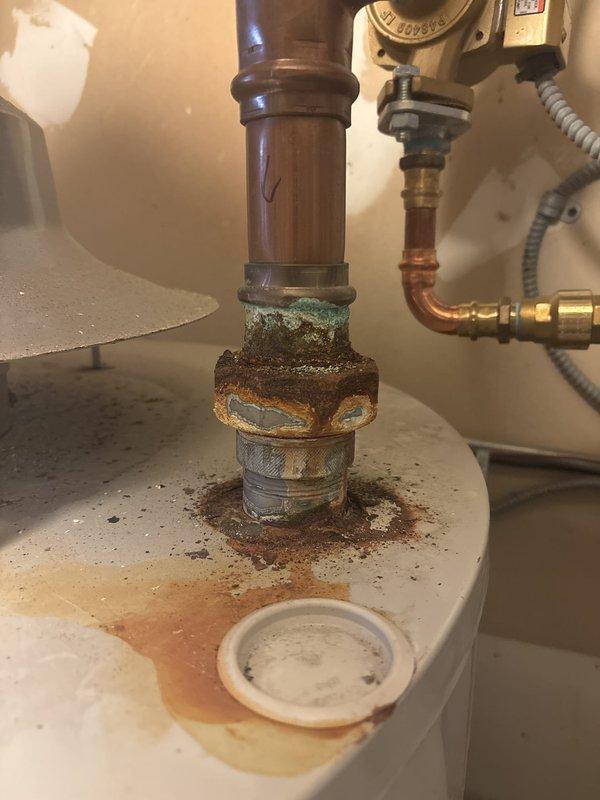 Inspected the water heater installation and found it noncompliant with code, with heavy corrosion at the hot outlet fitting and rust staining on the tank top indicating prior leakage. Corrected the installation by installing a 1-1/2" x 3/4" ProPress tee and a 1-1/2" dielectric union to isolate dissimilar metals, and added a thermal expansion tank set to 60 PSI on the water supply line.