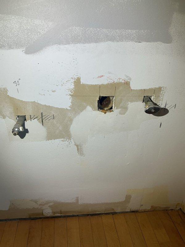 Accessed the in-wall plumbing at the repair location and documented the existing conditions, including multiple pipe penetrations through the drywall and a cut-out exposing a heavily corroded cast iron fitting with flaking rust and debris buildup. Marked layout reference lines on the wall for the planned repair work and surveyed the surrounding drywall and joint compound finish to assess the scope of the repair.