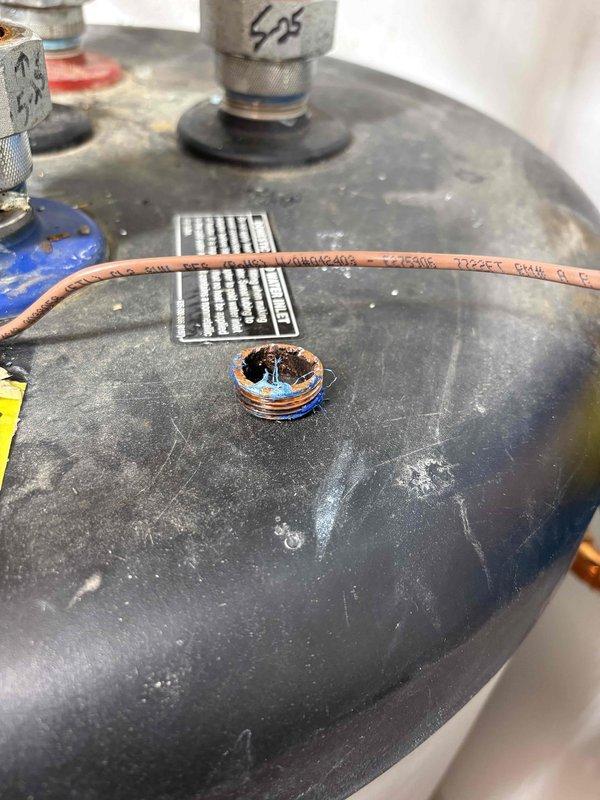 Assessed the water heater and mechanical room piping for a warranty repair estimate, documenting a heavily corroded threaded brass plug on the tank top with deteriorated thread sealant, along with the expansion tank, copper supply piping, and PVC connections, which showed no visible leaks, rust, or damage. Warranty replacement parts are on hand at the shop, and the repair is pending scheduling.