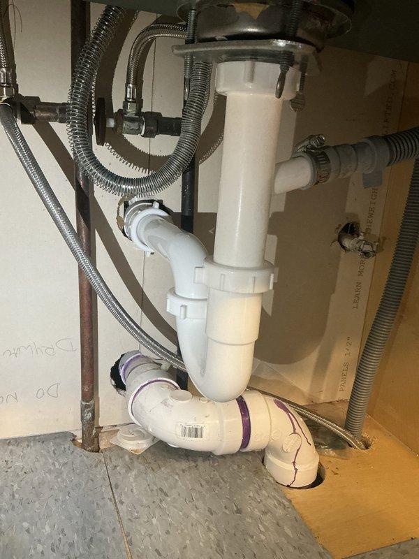Responded to a clogged kitchen sink where prior homeowner attempts to clear the P-trap were unsuccessful. Inspected the drain assembly beneath the sink, including the tailpiece, slip-joint connections, PVC P-trap, and horizontal run to the wall, and cleared the blockage to restore proper drainage. Noted heavy buildup and corrosion on the brass coupling nut at the tailpiece, along with the dishwasher drain hose connection at the branch fitting, and verified the drain assembly was reassembled and flowing freely.