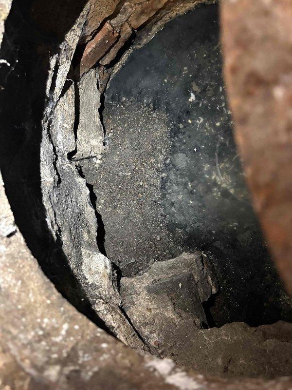 Inspected the reported sump pump issue and found the pit and surrounding structure in poor condition, with severely corroded metal at the rim, cracked and crumbling masonry walls, and a broken concrete slab at the base. Heavy sediment and debris buildup, along with murky sludge and a corroded pipe stub in the adjoining brick-lined passage, indicate deterioration that likely contributes to the pump's malfunction. Documented all findings with photos to support repair recommendations.