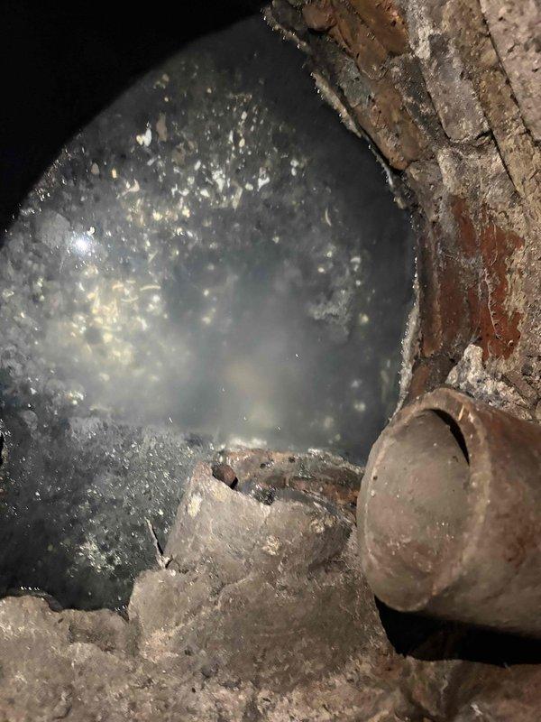 Inspected the reported sump pump issue and found the pit and surrounding structure in poor condition, with severely corroded metal at the rim, cracked and crumbling masonry walls, and a broken concrete slab at the base. Heavy sediment and debris buildup, along with murky sludge and a corroded pipe stub in the adjoining brick-lined passage, indicate deterioration that likely contributes to the pump's malfunction. Documented all findings with photos to support repair recommendations.