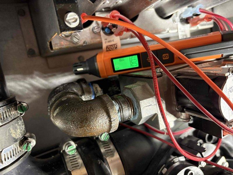 Responded to a persistent gas odor complaint and inspected the furnace gas train, including the black iron elbow and threaded connection to the gas valve, where corrosion and mineral residue were observed. Used a digital combustible gas detector to check the fittings, rubber couplings, and valve assembly for leakage and verify the source of the odor.