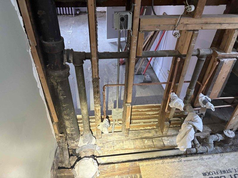 Performed an on-site estimate for replacement of the upstairs bathroom soil stack. Inspected the open wall and floor cavity, documenting the aged cast iron drain stack with banded couplings, heavy corrosion and staining, and adjacent drain branches and copper water supply lines that are capped and ragged off with recently soldered joints. Assessed the existing framing, subfloor condition, and surrounding demolition work to determine the scope of piping replacement and prepared the findings for quoting.