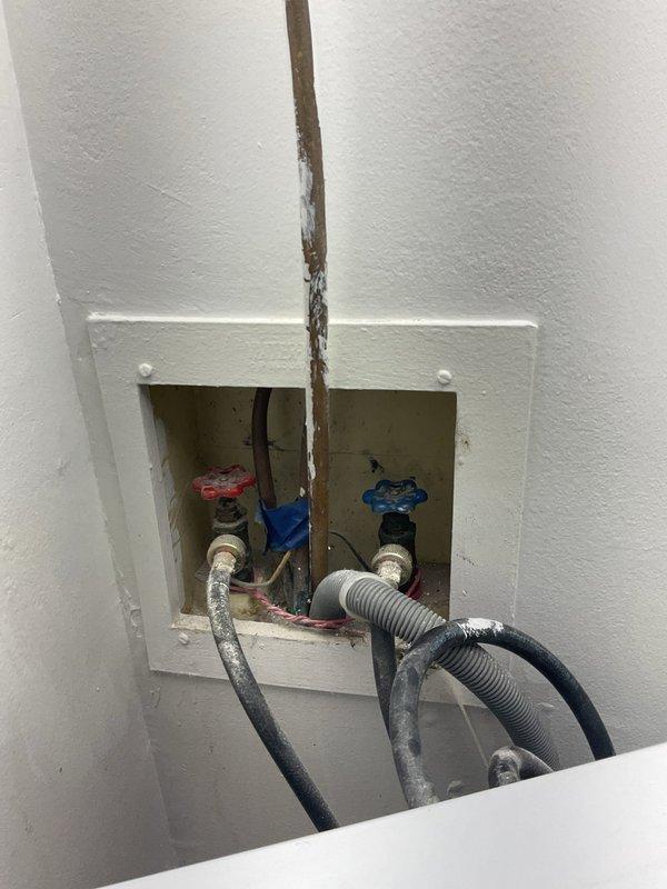 Inspected the recessed washing machine supply box and identified corroded supply piping with deteriorated paint and aged, dust-laden braided supply hoses at the hot and cold shutoff valves. Completed the sold repair at the washer connection, restoring secure, leak-free supply connections and verifying proper operation of the shutoff valves and drain hose routing.