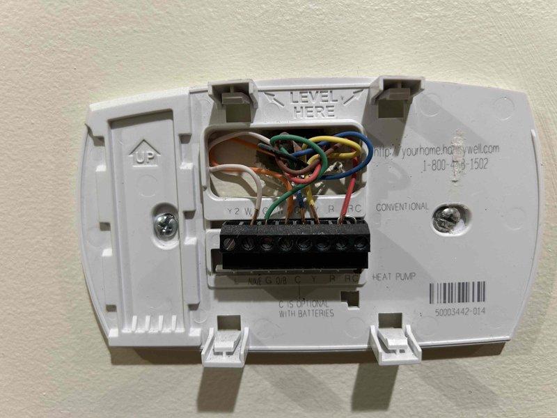 Diagnosed a no-heat issue on a 15-year-old electric heat pump system. Inspection revealed faulty wiring connections at the thermostat - removed and examined the Honeywell thermostat mounting plate to verify proper terminal connections. Also inspected the control board housing in the indoor unit located in basement, finding several loose wire connections which were secured. System tested operational after repairs with proper heating function restored.