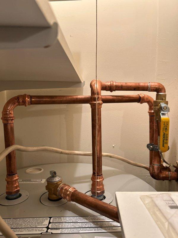 Installed new tanked water heater with proper elevation to accommodate drain pan and discharge system. Modified drywall behind washing machine to establish drainage connection. Connected copper supply lines with appropriate fittings and installed gas valve. Confirmed system functionality before completion.