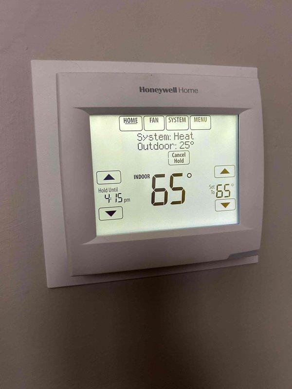 Responded to call back regarding heating and cooling system's inability to maintain target temperatures. Upon investigation, inspected Honeywell thermostat displaying proper readings (65° indoor/25° outdoor) and operating in Heat mode. Removed thermostat cover to examine wiring connections at terminal block, verifying proper wire placement and secure connections for red, yellow, green, and white wires. All components tested functioning correctly after service.