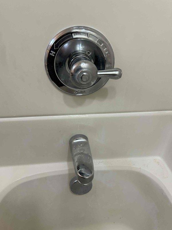Inspected leaking shower/tub fixture with chrome valve and handle assembly. Identified mineral buildup and wear on the escutcheon plate contributing to the leak. Repaired valve mechanism while maintaining access behind the wall-mounted components. Customer's shower remains functional following service completion.