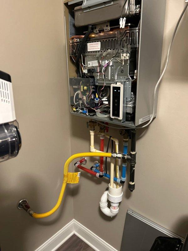 Performed assessment of Ruud tankless water heater (approximately 2 years old) that customer reports is approved for warranty replacement due to recurring issues. Visual inspection of the unit revealed intact internal components including circuit boards, wiring harnesses, heat exchangers, and proper gas line connections. Documented current installation configuration including PVC venting system, water line connections, and gas supply to facilitate proper reinstallation of warranty replacement unit when received from supplier.
