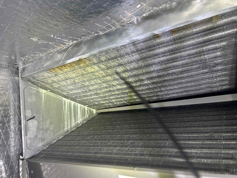 Performed routine Care Plan Tune Up on heat pump/air handler system located in garage. Visual inspection revealed significant buildup on evaporator coil with yellowish-green residue indicating possible mold or corrosion. Conducted electrical diagnostics using Fluke 376 FC clamp meter, measuring 7.9 amps at compressor. System operation verified after service.