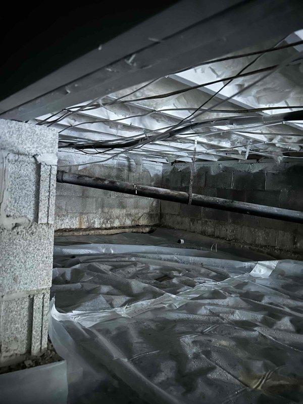 Performed inspection of main drain system in crawl space to investigate customer-reported odors, slow drains, and bubbling sounds. Customer suspected root intrusion in corrugated pipe section where drain line runs under driveway and discharges to creek. Inspected plumbing infrastructure and identified areas of concern in the vapor barrier protected basement area where multiple drain lines converge.