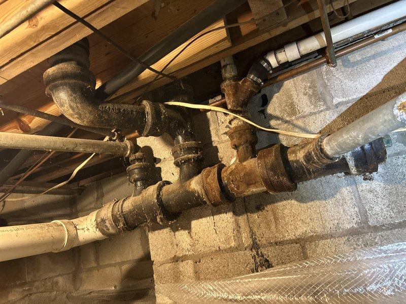 Conducted inspection of deteriorated galvanized piping system in crawl space requiring full replacement. Observed significant corrosion and rust on existing pipes mounted along wooden joists. Recommended complete replacement with PVC piping, including necessary connections to existing plumbing infrastructure serving laundry facilities.
