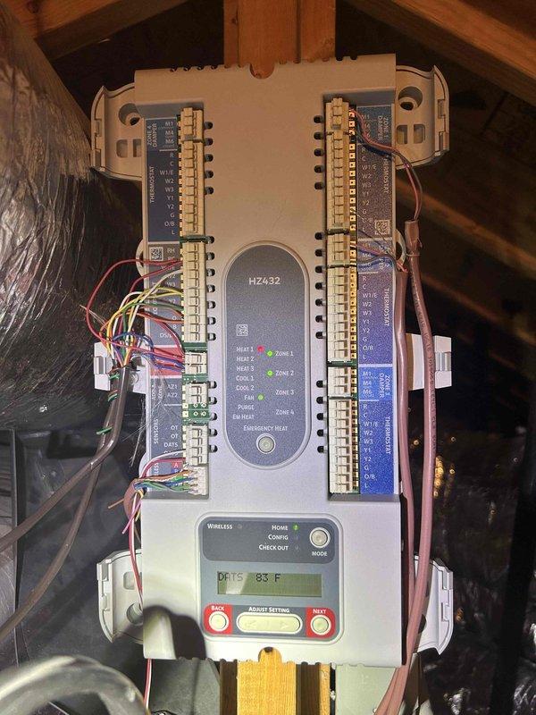 Diagnosed heat pump system experiencing intermittent no-heat condition. Verified Honeywell thermostat was properly calling for heat at 70°F setpoint but system was delivering cool air despite indicating auxiliary heat mode. Inspection of zone controller (HZ432) in attic revealed improper sequencing between primary and auxiliary heat stages. Recalibrated staging parameters and verified proper discharge air temperature (83°F) at zone 1. System now operating correctly with appropriate heat delivery.