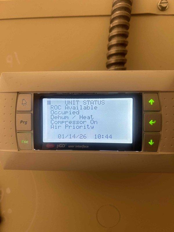 Responded to IAQ service call for a whole home humidifier issue with reported coil problems. Inspected outdoor HVAC unit with dual fan configuration and associated drainage system. Examined digital control panel which displayed "Dehum - Heat" and "Compressor On" status indicators, confirming system was actively running dehumidification cycle with compressor engagement.