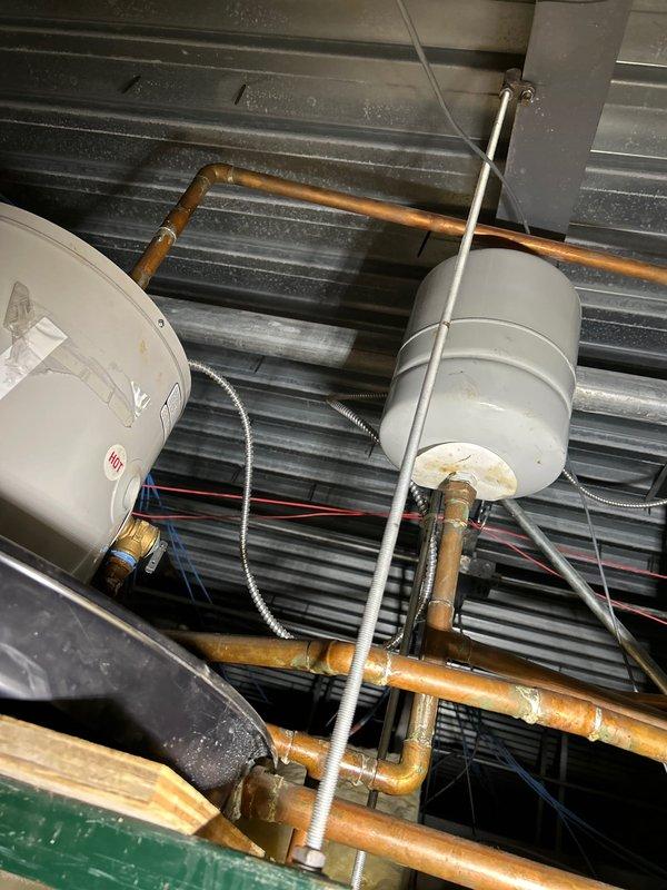 Inspected ceiling-mounted commercial water heater system in break room. Identified aging expansion tanks and copper piping with significant oxidation. Unit (approximately 10 gallons) was non-operational with no hot water output. Documented condition with photos showing deteriorated components and installation configuration for further assessment.