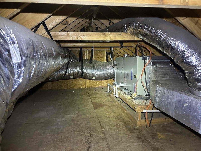 Conducted site evaluation for media cabinet installation request. Inspected existing HVAC system components including wall-mounted air handler with flexible ductwork and drain lines. Examined attic space containing main unit mounted on wooden platform with insulated silver ductwork running throughout. Documented current configuration with photos for estimate preparation.