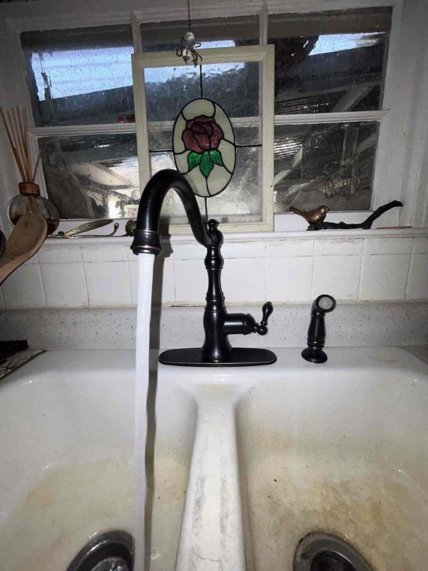 Successfully installed customer-supplied kitchen faucet with new supply lines, replacing the previous black faucet with curved neck and separate spray attachment. Completed all connections to existing water system, tested operation thoroughly, and verified zero leaks upon completion.